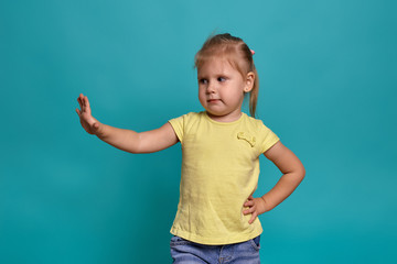 Close-up studio shot of a beautiful little girl. Little blonde girl in a yellow T-shirt on a blue background. The emotions of a child.