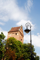 An old brick tower and a lantern against a background of green thickets and blue sky. The urban landscape in Warsaw, Poland.