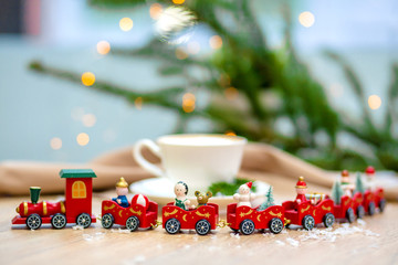 Delicious fresh festive morning cappuccino coffee in a ceramic white cup on the wooden table with decorative christmas train, red ornamentals, fireflies and spruce branches