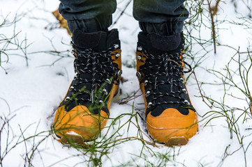 Male legs wearing hiking brown shoes in snow at nature.