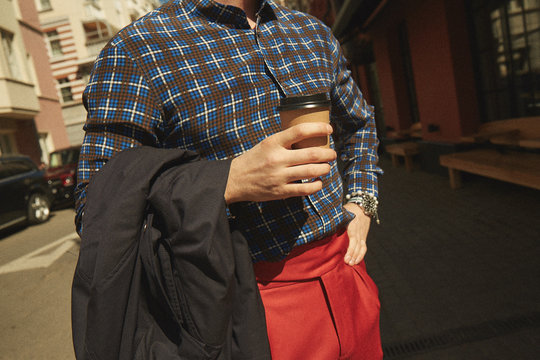 A modern stylish man standing with a paper cup of coffee on a street in the city