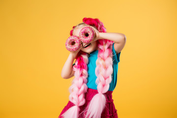 little girl with donuts on yellow background isolate, space for text