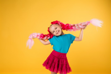 little girl with braids of pink kanekalon on a yellow background isolate