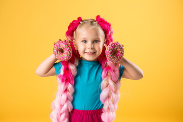 little girl with donuts on yellow background isolate, space for text