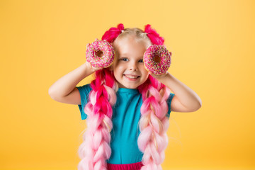 little girl with donuts on yellow background isolate, space for text