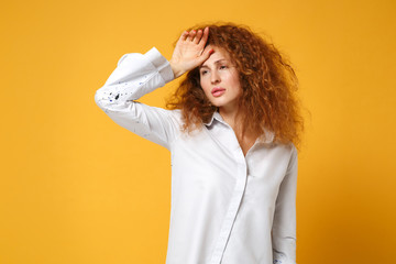 Exhausted tired young redhead woman girl in white shirt posing isolated on yellow orange wall background, studio portrait. People lifestyle concept. Mock up copy space. Putting hand on head crying.