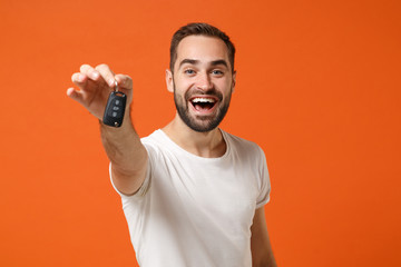 Excited young man in casual white t-shirt posing isolated on bright orange wall background studio portrait. People sincere emotions lifestyle concept. Mock up copy space. Holding in hand car keys.