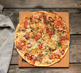 baked round pizza with smoked sausages, mushrooms, tomatoes, cheese