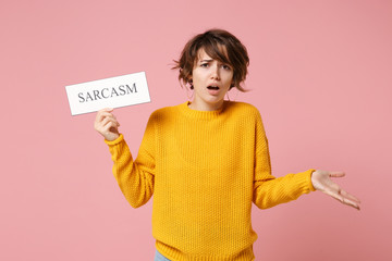 Displeased young brunette woman girl in yellow sweater posing isolated on pastel pink wall background. People lifestyle concept. Mock up copy space. Holding sign with CENSORED title, spreading hands.