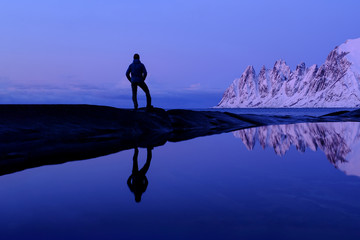 Man standing at Tungeneset, his mirror reflection in the water, mountains in the background, Senja, Troms, Norway