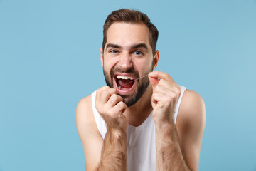 Bearded young man 20s years old in white shirt hold using dental floss isolated on blue pastel wall background studio portrait. Skin care healthcare cosmetic procedures concept Mock up copy space.