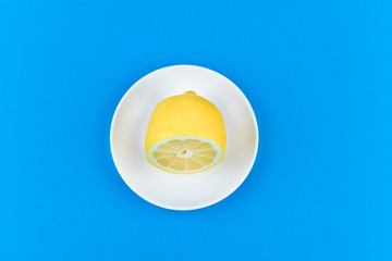 Obraz na płótnie Canvas lemon on a blue background. lies on a white plate. half cut lemon. view from above. place to record. Lemon slices on a blue background. In summer, cool slices of orange. Lime, fruit, refreshing, yello