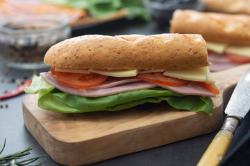 Sandwich with baguette bread, ham, lettuce, tomatoe over dark background. Breakfast or fast food.