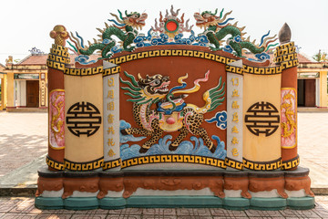 Obraz premium Nha Trang, Vietnam - March 11, 2019: Dinh Phu Vinh community center and celebration hall. Decorative beige and maroon short wall with Dragon fresco and statues under silver sky.