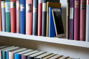 Mobile phone standing upright between books in bookcase