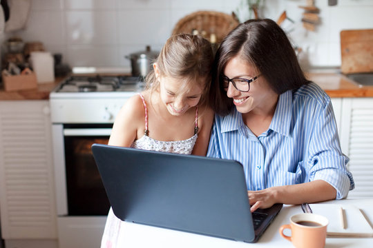 Holiday shopping online. Happy mother and child girl make purchases in the Internet on Black Friday. Cute kid and woman are smiling. Family are enjoying buying gifts with laptop in cozy home kitchen. - Powered by Adobe