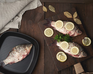 fresh crucian fish sprinkled with spices and lemon slices and lies on a brown wooden cutting board