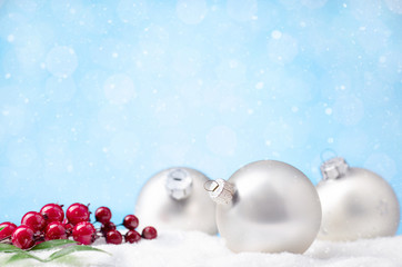 christmas balls on snow with branch of holly berry on blue background