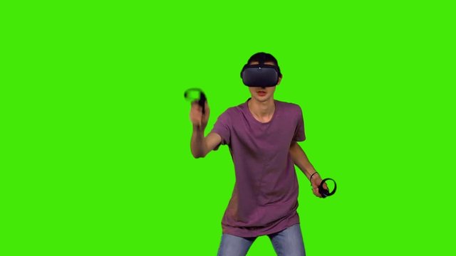 Slow motion, teenage boy with a VR headset playing a game in a medium shot over green screen.