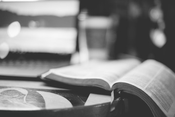 Grayscale closeup shot of an open bible on the table wit ha blurred background