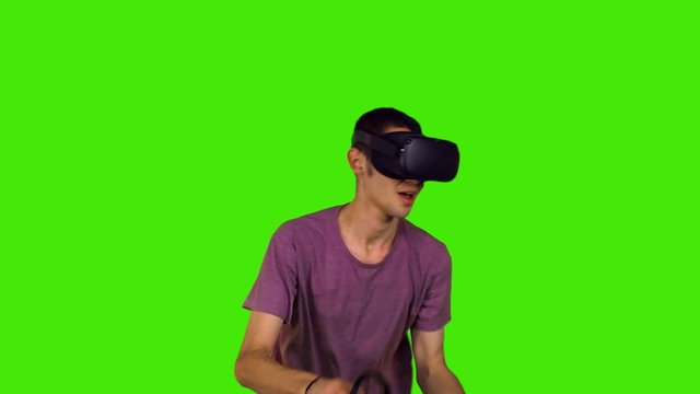 Slow motion, teenage boy with a VR headset playing a game and smiling in a medium shot over green screen.