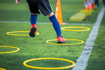Selective focus to kid soccer player Jogging and jump at ring ladder marker on green artificial turf. Equipment for training class of football academy.