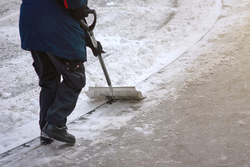 Worker shoveling snow on sidewalk after heavy snowfall. Municipal city service cleans footpath from snow and ice after blizzard. Janitor holds metal snow shovel in his hand and sweep snow from road