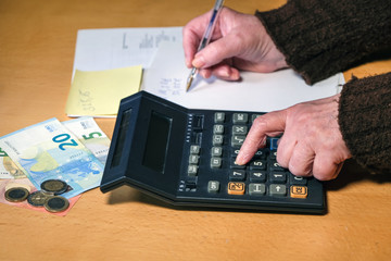 Ã„ltere, arme Frau zÃ¤hlt Geld mit einem alten Taschenrechner zusammen und macht sich Notizen...