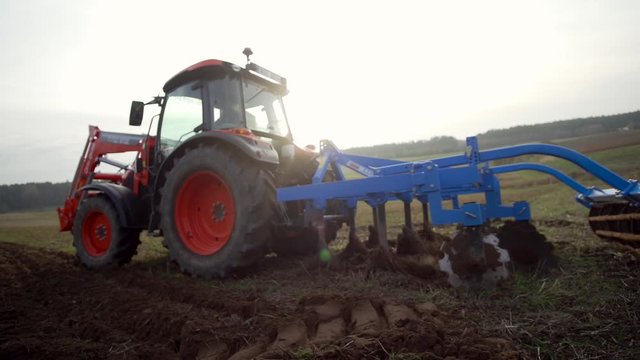Tractor lowering farm machinery plough into dirt soil farmland preparing to turn dirt ground for harvesting cultivation.