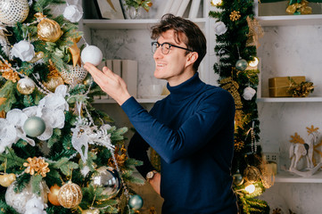 Happy handsome man decorating cristmas tree in cozy room with new year holidays decorations.
