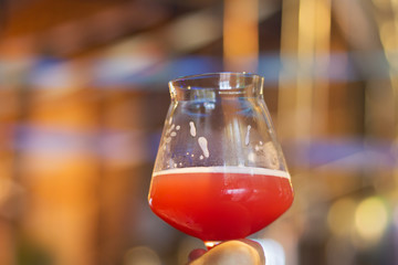 A glass of craft beer with infused raspberry flavor during testing event in Burlington, Vermont, USA. Background hues of festive autumn atmosphere in a bar. - 301862248