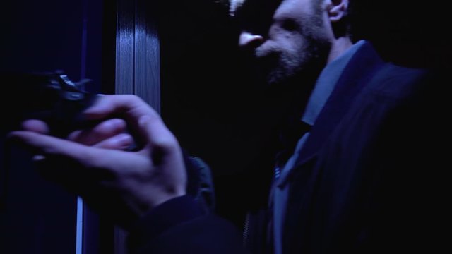 Cautious policeman entering dark room with handgun, examining nest of criminals