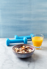 Bowl of granola with nuts, raisins, cranberries and chia seeds. Blue dumbbells in background. Concept for a tasty and healthy meal. Stone - wooden background. Copy space.