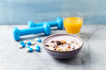 Bowl of granola with yogurt, nuts, raisins, cranberries and chia seeds. Blue dumbbells and sports supplements in background. Concept for a tasty and healthy meal. Stone - wooden background. Close up.