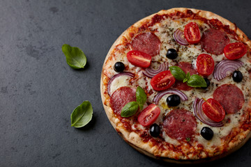 Pizza with salami, mozzarella cheese, cherry tomatoes, black olives, red onion and oregano. Home made food. Concept for a tasty and hearty meal. Black stone background. Close up. Copy space