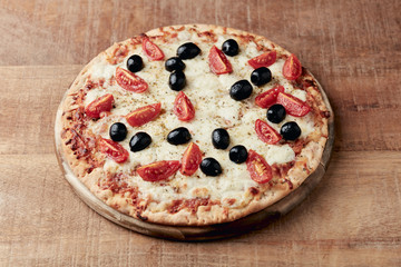 Pizza with mozzarella cheese, cherry tomatoes, black olives and oregano. Home made food. Concept for a tasty and hearty meal. Rustic wooden background. Copy space. 