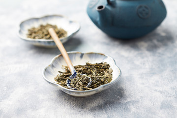 Dried Green Tea Leaves and Iron Tea Pot on bright wooden Background. Close up. Copy space. 