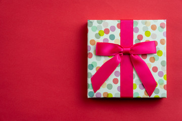 Flat lay a single polka dots gift box with ribbon isolated on red background.
