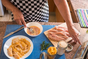 Front view of a female hands preparing the chicken nuggets to be fried. Looking the recipe on the tablet next to her.