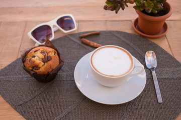 A rustic wooden table ready for the breakfast with a hot cappuccino, and a fresh croissant.