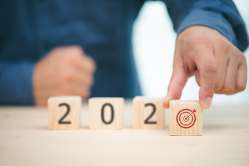 businessman hand holding wood wooden cubes with New year 2020 and target icon. goal concept in 2020.