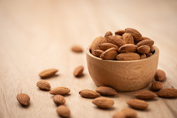 Almonds in wood bowl on light wood table. Almond concept with copyspace.
