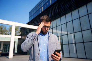 Male business person looking at mobile phone and holding coffee cup