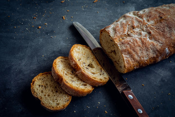 Bread loaf sliced with knife on dark background.
