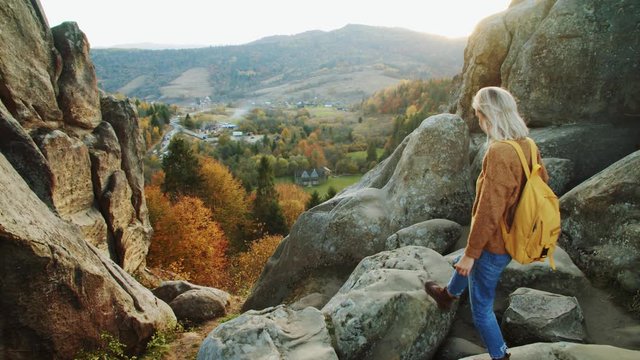 Female blonde tourist exploring gorgeous mountains hills high above countryside. Adventurous free young woman enjoying freedom nature scenery from cliff top at fall season.