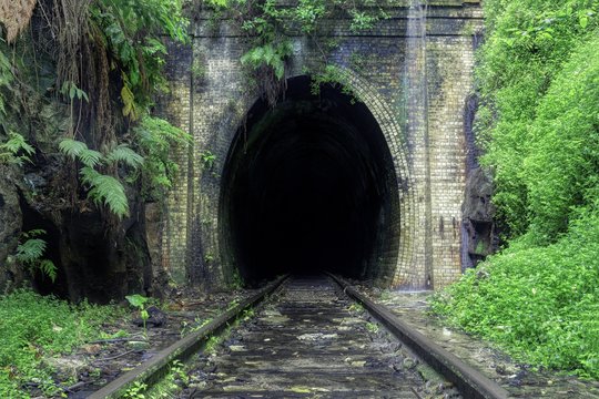 Fototapeta Beautiful shot of train rails surrounded by nature leading to the dark tunnel