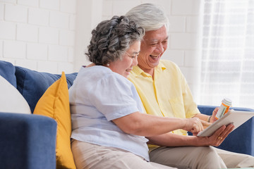 Asian senior couple use tablet video conference with doctor about pill  while sitting on sofa at home,senior learn to use technology.aging at home - obrazy, fototapety, plakaty