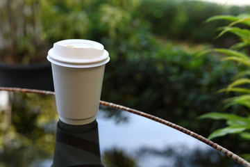 take away cup for hot coffee drink put on glass table inside garden cafe in the morning day
