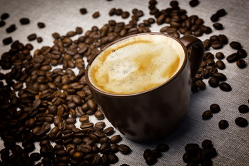 Cup of coffee and sprinkled coffee beans on burlap