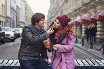 Fototapeta na wymiar Portrait of beautiful young couple eating Trdelník in the street. Having fun in winter of the european city. Vacation and holiday concept